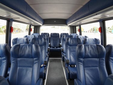 Spacious interior cabin of a luxury tour bus, featuring clean leather reclining seats, individual USB ports, and modern air conditioning vents, bright natural daylight